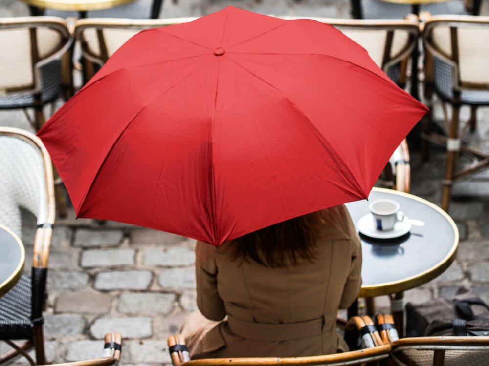 Parasolka LEXON Mini Hook LU21LB1 Jasnoniebieski osoba siedzi na krześle zasłonięta czerwonym parasolem 50 x 122 x 50 cm z wytrzymałych materiałów ABS aluminium poliester niewielkie rozmiary zmieści się w torbie w plecaku do codziennego noszenia zawsze pod ręką funkcjonalna stylowa w miejskich warunkach 