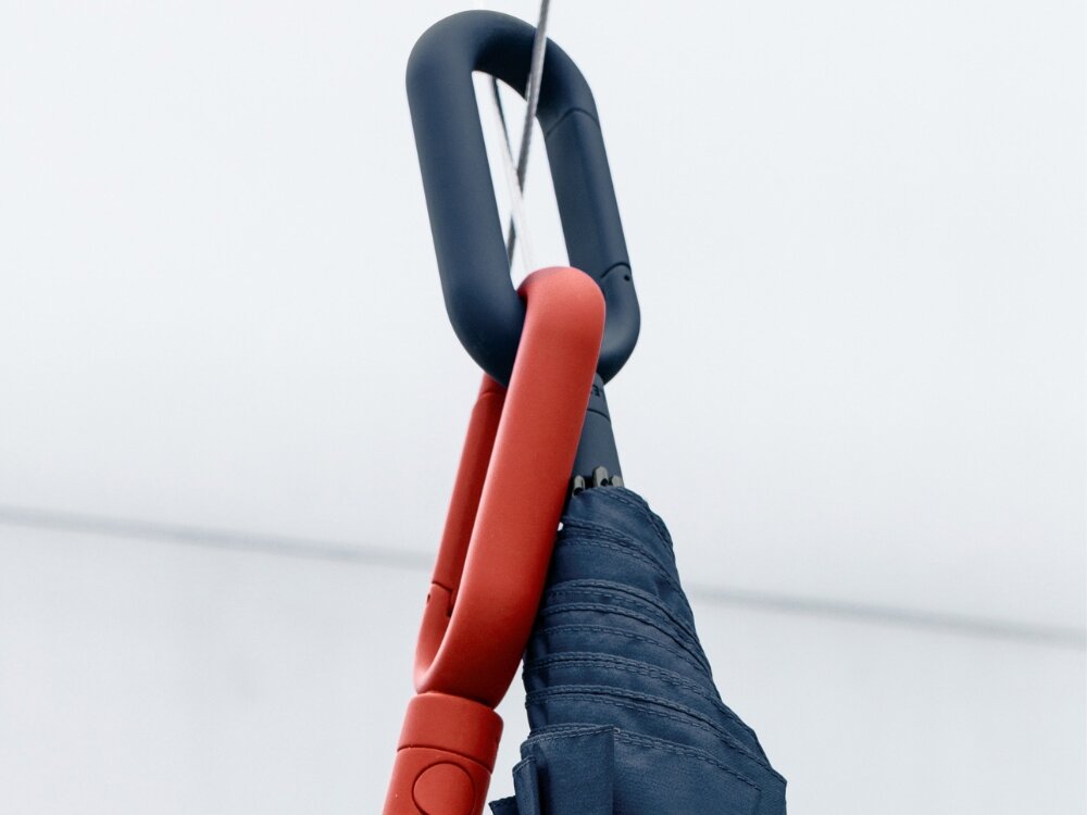 Parasolka LEXON Mini Hook LU21LB1 Jasnoniebieski jasne tło czerwony i granatowy karabińczyk zamontowane o siebie Karabińczyk wbudowany w uchwyt parasola zwiększona wygoda użytkowanie na pasku torby uchwycie plecaka haczyku w szatni przy wieszaku w przedpokoju zawsze pod ręką nie zajmuje dodatkowego miejsca funkcjonalny detal