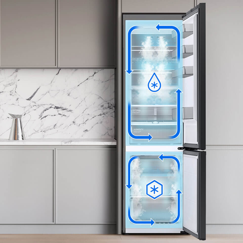 Otwarta lodówka z widocznymi strzałkami wskazującymi przepływ powietrza i symbolami kropli oraz płatka śniegu. W tle znajduje się kuchnia z marmurowym blatem i szafkami.