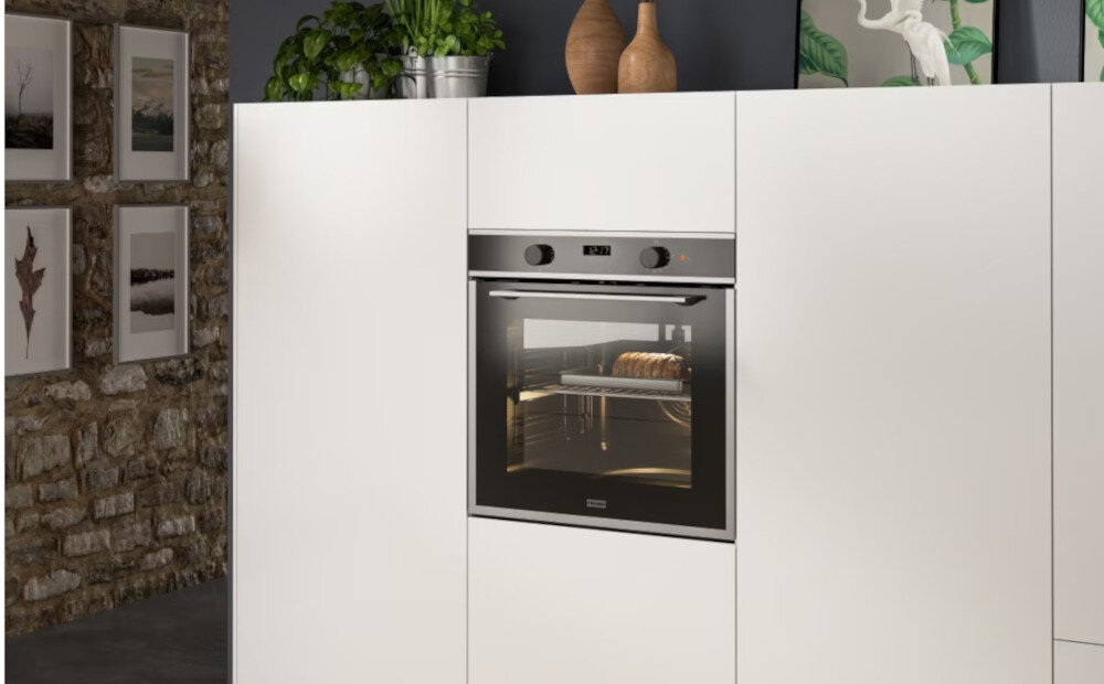 Piekarnik FRANKE Maris FMA 86 H XS Widok z boku pokazuje piekarnik z uchylonymi drzwiczkami w stylowej kuchni. W tle widoczne jest duże okno doświetlające pomieszczenie