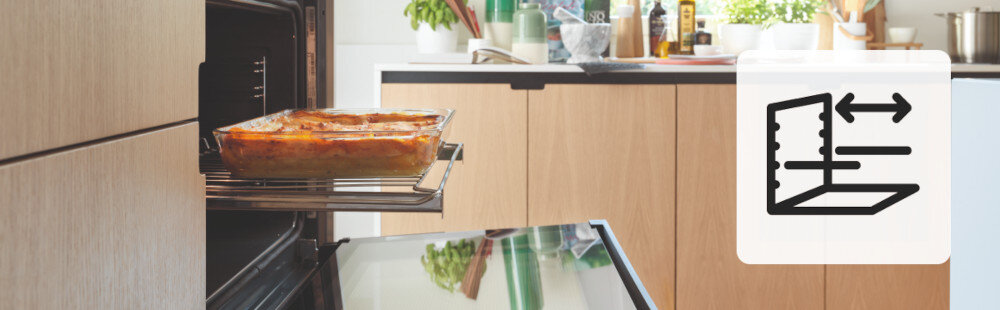 Piekarnik FRANKE FSL 86 H BK Na zdjęciu widać otwarty piekarnik z wysuniętą prowadnicą teleskopową, na której stoi żaroodporne naczynie z zapiekanką. W tle znajduje się kuchnia z drewnianymi frontami. Po prawej stronie widoczna jest ikona przedstawiająca symbol prowadnic teleskopowych prowadnice teleskopowe płynne wysuwanie wygodne pieczenie bezpieczeństwo