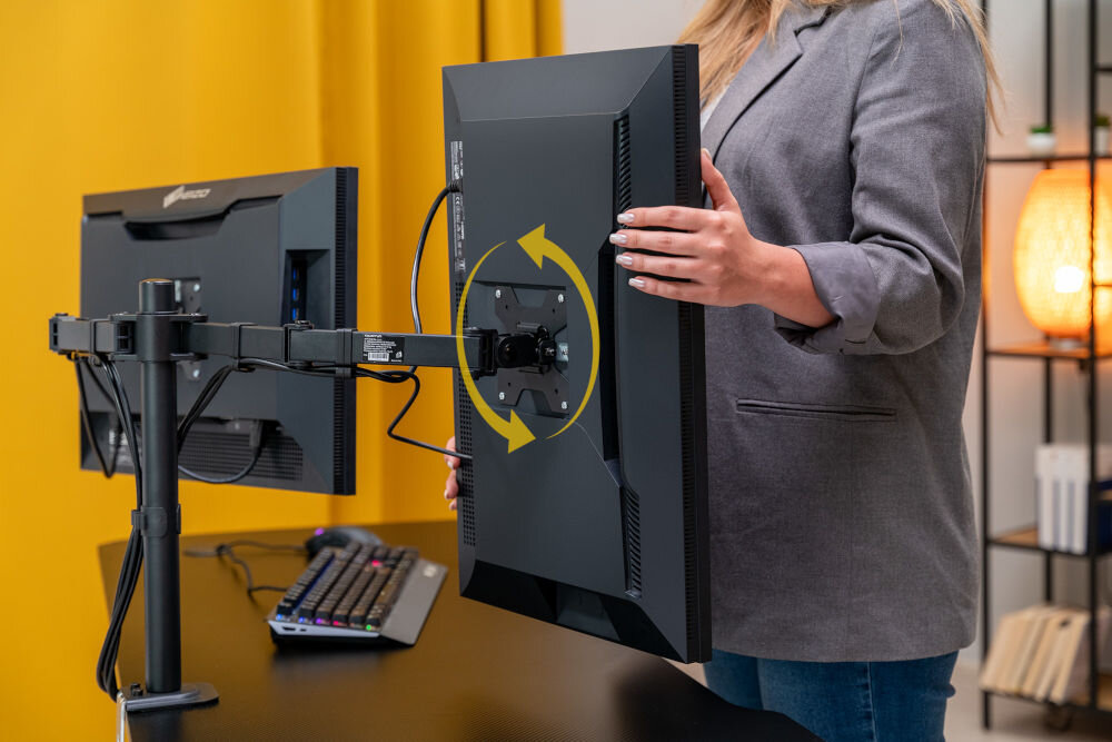 Uchwyt XQUANTUM MA10322 Osoba prezentująca funkcję obrotu (pivot) monitora zamontowanego na uchwycie xquantum. Na zdjęciu widoczna żółta strzałka symbolizująca ruch ekranu z orientacji poziomej do pionowej.