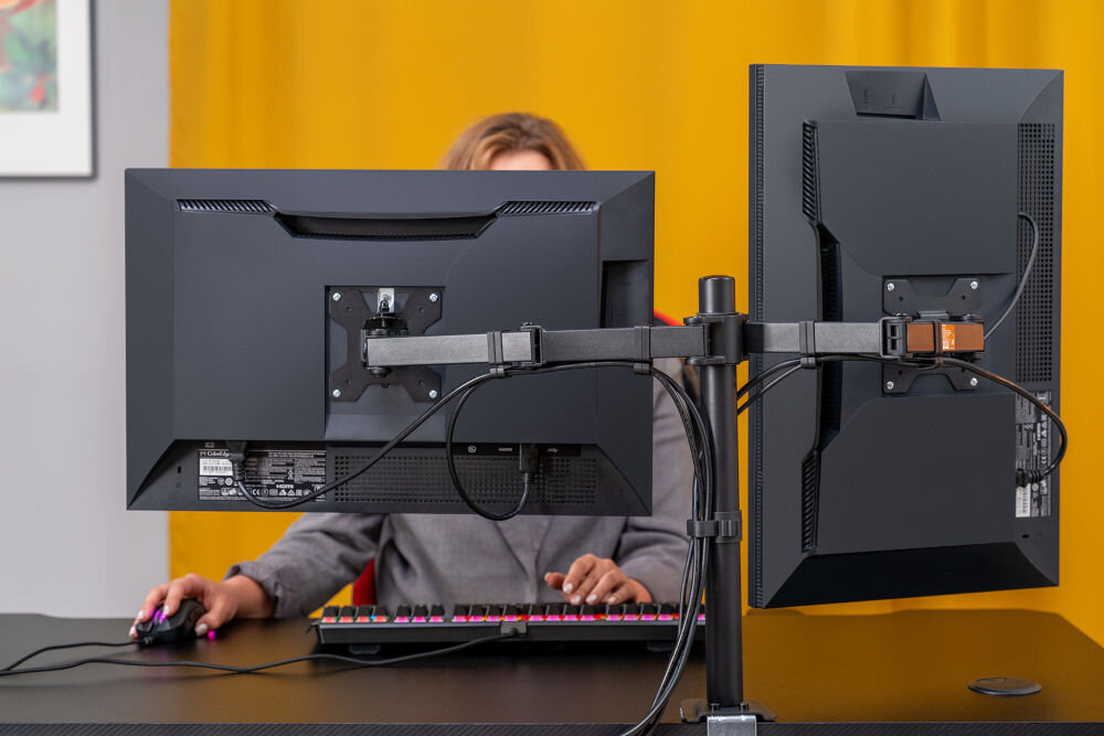 Uchwyt XQUANTUM MA10322 Widok z boku na biurko z monitorem ustawionym pionowo na uchwycie xquantum. Osoba trzyma ekran obiema rękami, demonstrując stabilność i łatwość regulacji pozycji wyświetlacza.