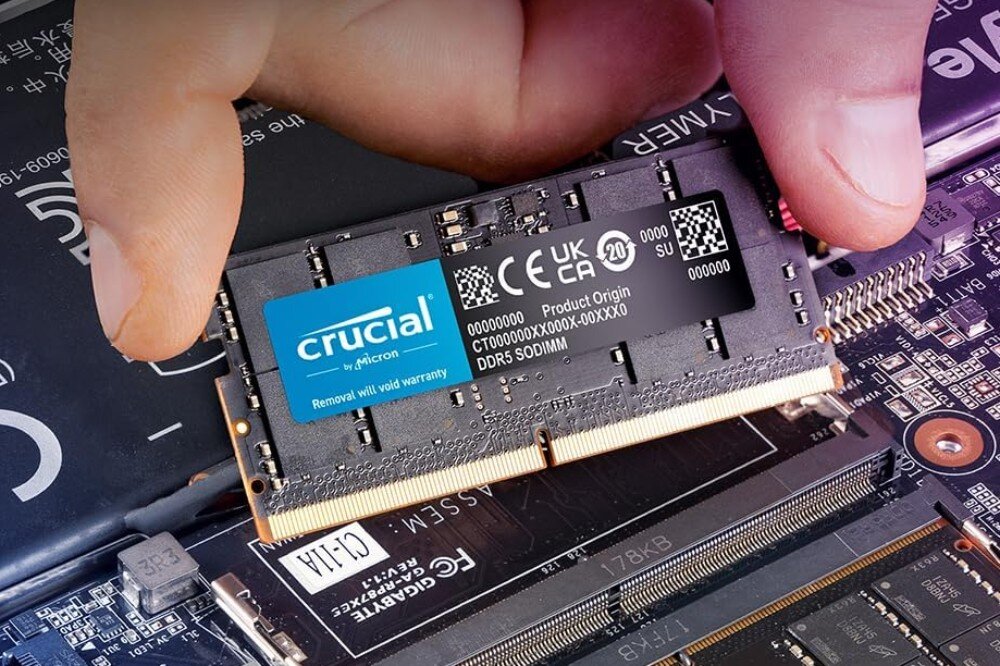 Pamięć RAM CRUCIAL 64GB (2x32GB) 4800MHz CT2K32G48C40S5 Zbliżenie dłoni montującej czarny moduł pamięci SODIMM w gnieździe laptopa na płycie głównej