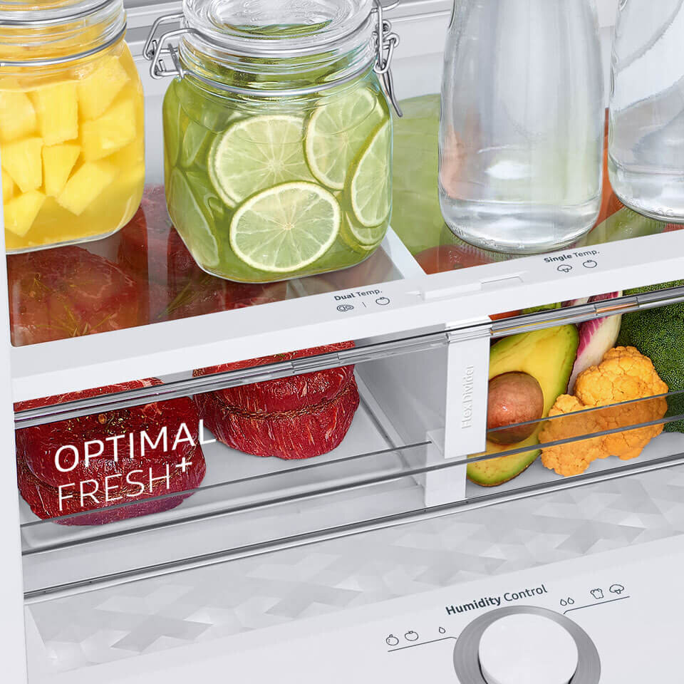 Wnętrze lodówki z widocznymi półkami, na których znajdują się słoiki z pokrojonymi owocami i butelki z wodą. Na szufladzie widoczny jest napis \'OPTIMAL FRESH+\'.