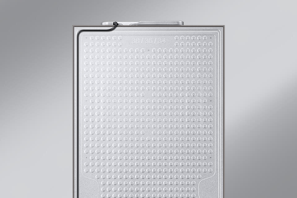 Srebrna powierzchnia z wypukłymi okrągłymi wzorami i widocznym cienkim przewodem w górnej części. Na powierzchni znajduje się tekst: \'23 / PB / 2a\'.