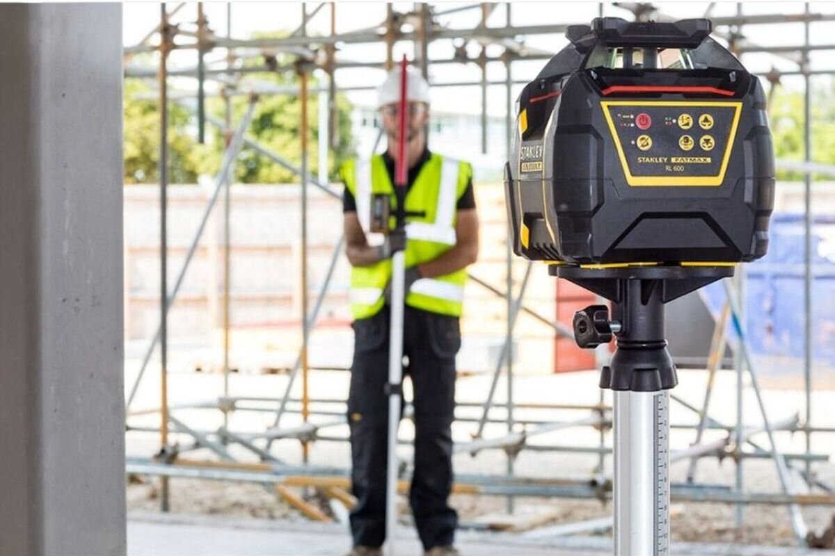 Laser rotacyjny STANLEY FMHT77446-1, rotacja, zasięg, poziom, pion, Stanley Fatmax RL 600 na statywie, w tle pracownik na budowie.