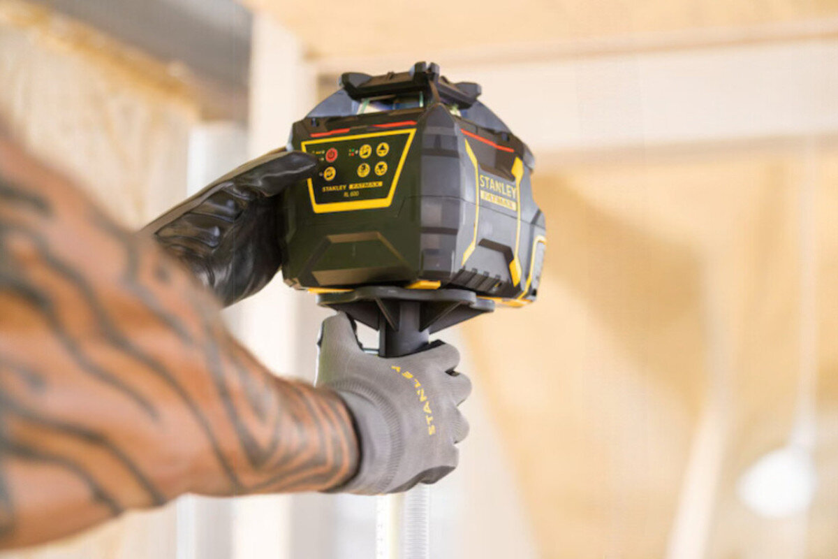 Laser rotacyjny STANLEY FMHT77446-1, laser, detektor, dokładność, rotacja, Zbliżenie na dłoń pracownika obsługującą panel sterowania niwelatora Stanley Fatmax.