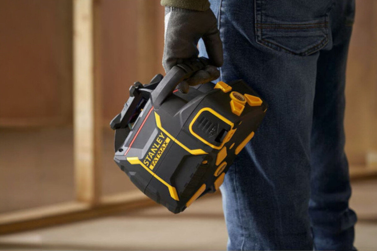 Laser rotacyjny STANLEY FMHT77446-1, baterie, czas, wskaźnik, przyciski, Pracownik przenosi niwelator laserowy Stanley Fatmax za zintegrowany uchwyt.