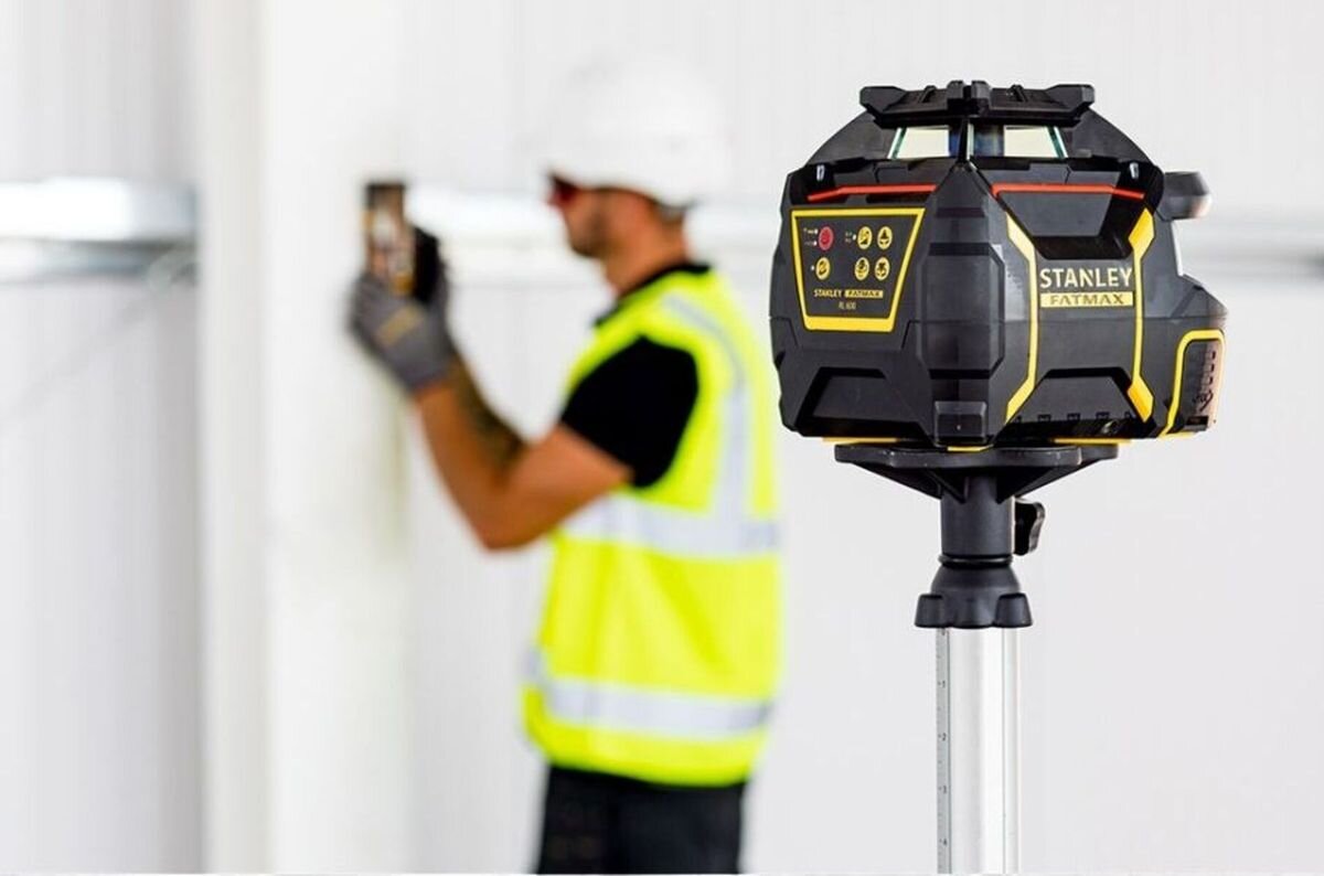 Laser rotacyjny STANLEY FMHT77446-1, regulacja, plumb, diody, libella, Stanley Fatmax RL 600 na pierwszym planie, w tle pracownik z łatą pomiarową.