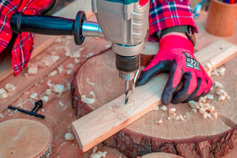 Wiertarka udarowa TRYTON TDW1050A pomieszczenie drewniany blat roboczy osoba wkręca się w drewnianą deskę dwa biegi na pierwszym biegu prędkość wynosi 0–1200 obr./min drugi bieg osiąga 0–3200 obr./min kontrola i efektywność pracy wierci w drewnie do 40 mm w stali do 13 mm w betonie do 20 mm