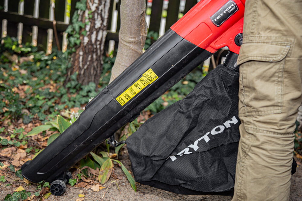 Dmuchawa do liści TRYTON TOE3000 elektryczna ogród drzewa krzewy bluszcz osoba zmiata liście z ziemi wygodne przełączanie między trybem dmuchawy a odkurzacza poprawia ergonomię pracy efektywne planowanie czasu poziom hałasu wynosi 104 dB