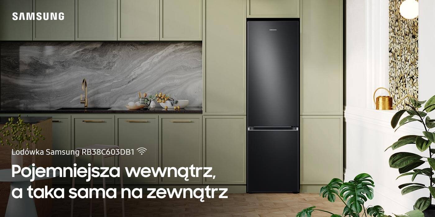 Lodówka z serii Grand + Samsung RB38C603DB1 dostępna w Media Expert Grafitowa lodówka Samsung RB38C603DB1 stoi w eleganckiej kuchni z zielonymi szafkami i marmurowym blatem. Na obrazie widoczny jest tekst: \'Lodówka Samsung RB38C603DB1 Pojemniejsza wewnątrz, a taka sama na zewnątrz\'.