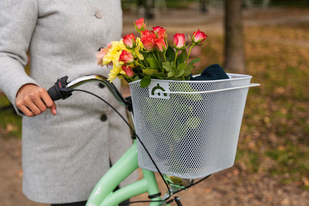 Koszyk na rower VÖGEL VKS-106 Stalowy Biały stalowy koszyk rowerowy przedni Vogel VKS-106 zamontowany na miętowym rowerze miejskim, wypełniony bukietem róż