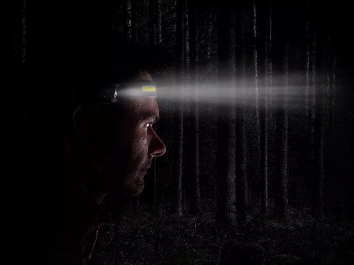 Latarka czołowa NEO 1 99-097, jasność, mobilność, wygoda, precyzja, osoba w ciemności podczas deszczu oświetla drogę przed sobą