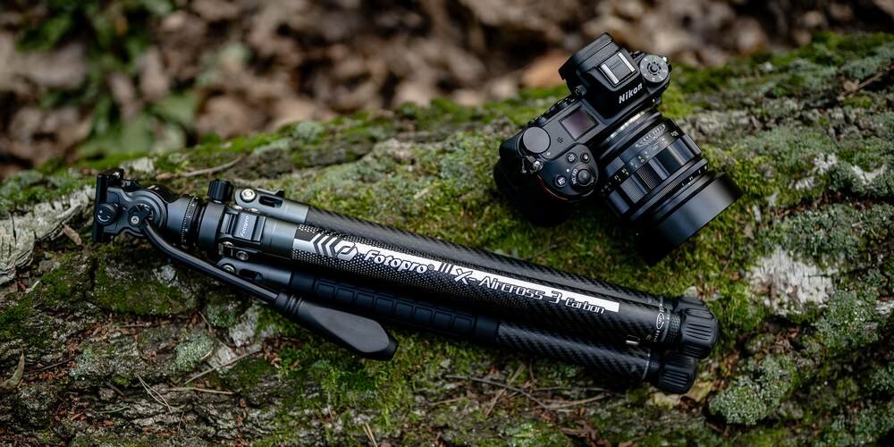 Aparat Nikon oraz statyw Fotopro X-Aircross 3 Carbon leżą na omszałym pniu drzewa w lesie, gotowe do sesji fotograficznej