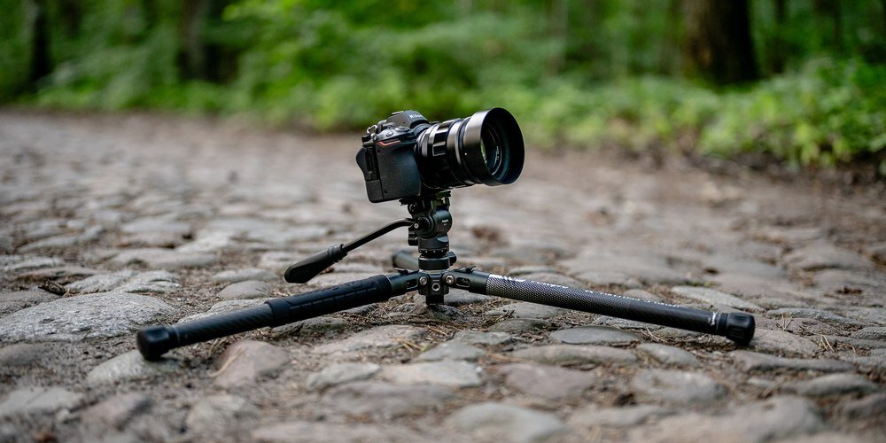 Aparat na nisko rozstawionym statywie Fotopro ustawiony na brukowanej drodze w lesie