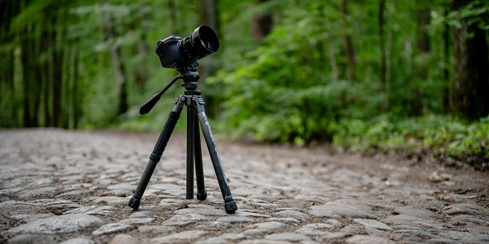 Aparat na statywie Fotopro X-Aircross 3 ustawiony na brukowanej drodze w lesie; statyw złożony do jednej sekcji nóg
