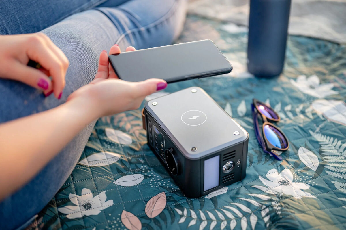 Stacja zasilania NEWELL Asvala Mini 88.8 Wh Bank energii, zasilanie, prąd, ładowanie, energia, stacja stoi na kocu, obok osoba trzyma w ręku smartfona