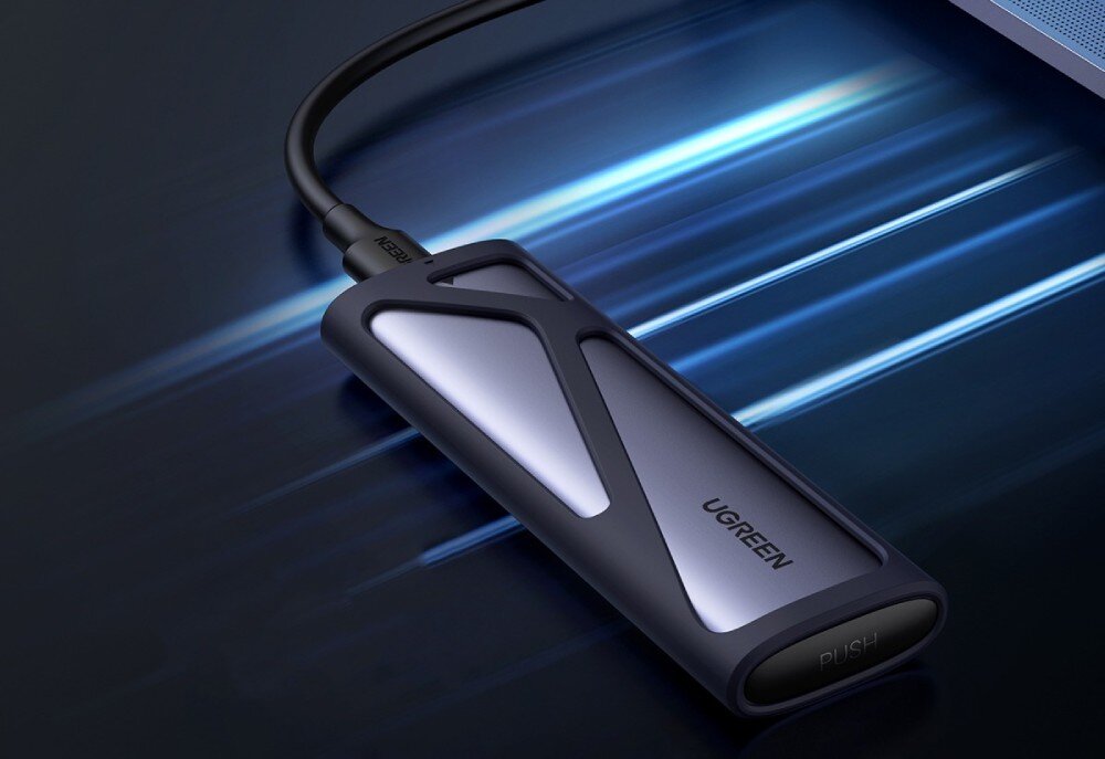 Obudowa dysku UGREEN CM400 Obudowa na dysk podłączona czarnym kablem do laptopa na ciemnym tle z rozmytymi pasmami niebieskiego światła