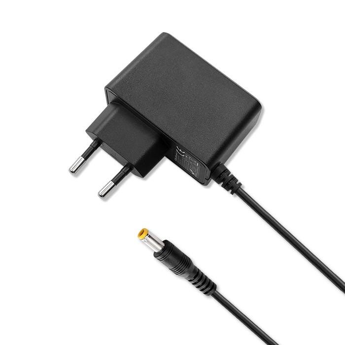 Na obrazie widoczny jest czarny zasilacz sieciowy z wtyczką oraz przewodem zakończonym żółtą końcówką. Zasilacz ma standardowe bolce do gniazdka elektrycznego.