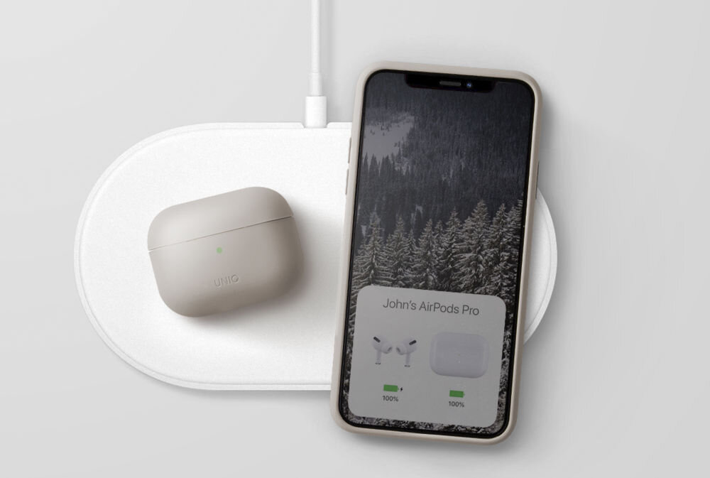 Na białej ładowarce bezprzewodowej znajduje się beżowe etui na słuchawki z logo \'UNIQ\' oraz smartfon z wyświetlaczem pokazującym las i tekst \'John\'s AirPods Pro\'.