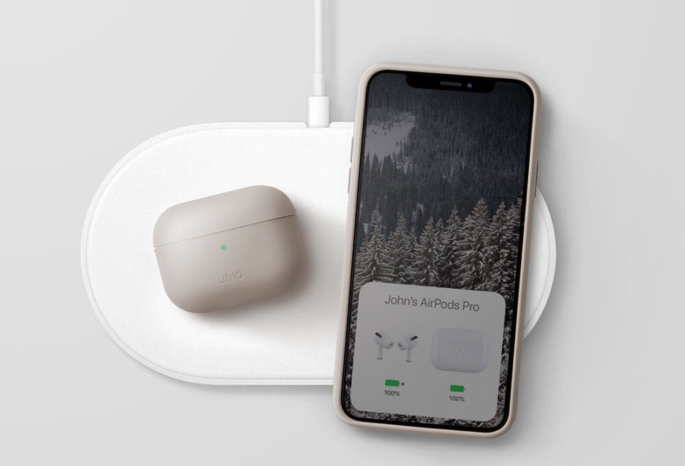 Na białej ładowarce bezprzewodowej znajduje się beżowe etui na słuchawki z napisem \'uniq\' oraz smartfon z wyświetlaczem pokazującym las i tekst \'John\'s AirPods Pro\'.