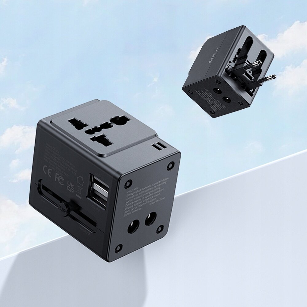 Na obrazie widoczne są dwa czarne adaptery podróżne z różnymi wtyczkami i portami USB. W tle znajduje się niebo z chmurami.