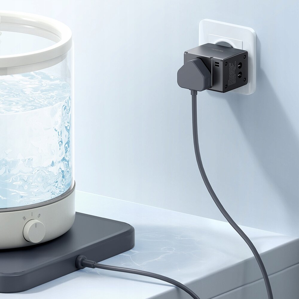 Na obrazie widać adapter podłączony do gniazdka elektrycznego, z którego wychodzi kabel. Obok znajduje się przezroczysty pojemnik z wodą na podstawce z pokrętłem.