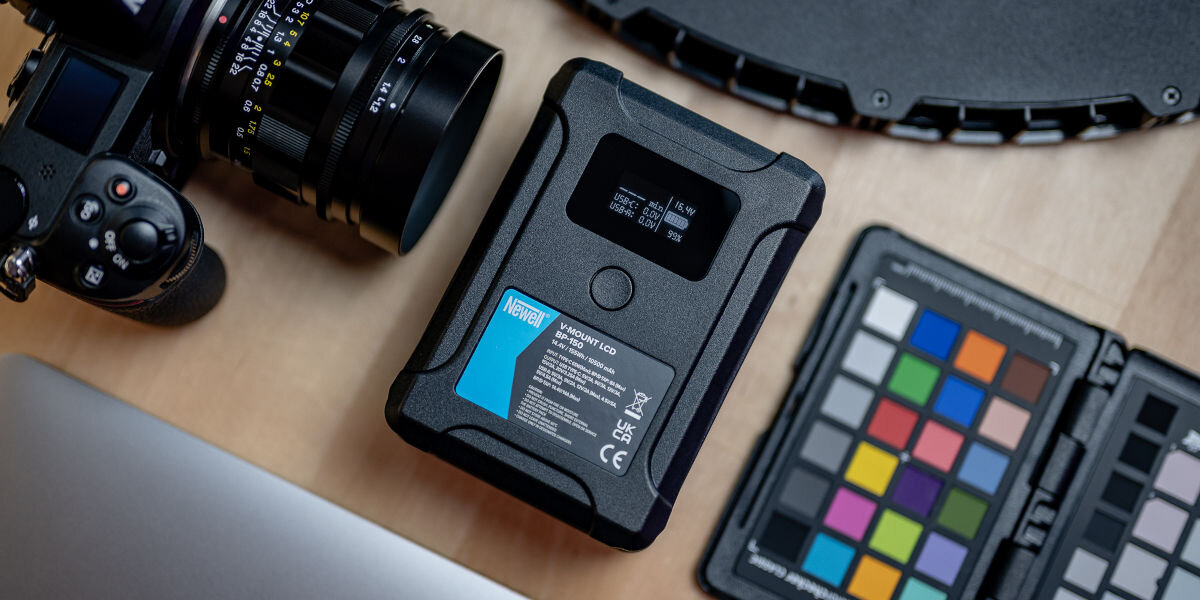 Akumulator NEWELL 10500 mAh do BP-150 LCD V-Mount, pojemność, porty, usb, LCD, akumulator leży na blacie wraz z różnymi modelami produktów elektronicznych