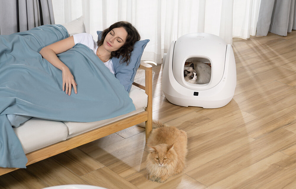 Inteligentna kuweta dla kota CATLINK Baymax kobieta śpi na podłodze leży rudy kot w białej kuwecie leży jasny kot trzy tryby pracy automatyczne czyszczenie tryb manualny zaplanowanie harmonogramu czyszczenia czystość na wysokim poziomie