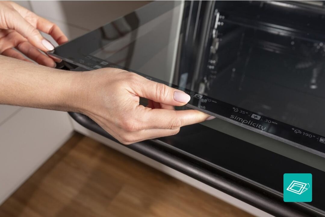 PIEKARNIK GORENJE BOS67371SYB Czyszczenie wewnętrznej strony drzwi piekarnika przy użyciu ściereczki, przy całkowicie otwartym froncie. Ujęcie podkreśla łatwy dostęp i prostą pielęgnację gładkiej szklanej powierzchni