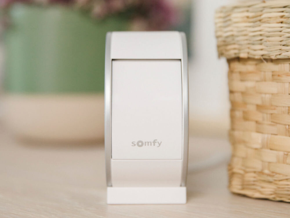 Kamera SOMFY Protect Wewnętrzna, Wi-Fi, wyjazdy, rozwiązanie. dostęp, nagrania, zbliżenie na kamerę na komodzie od frontu na wprost z zakrytą kamerką