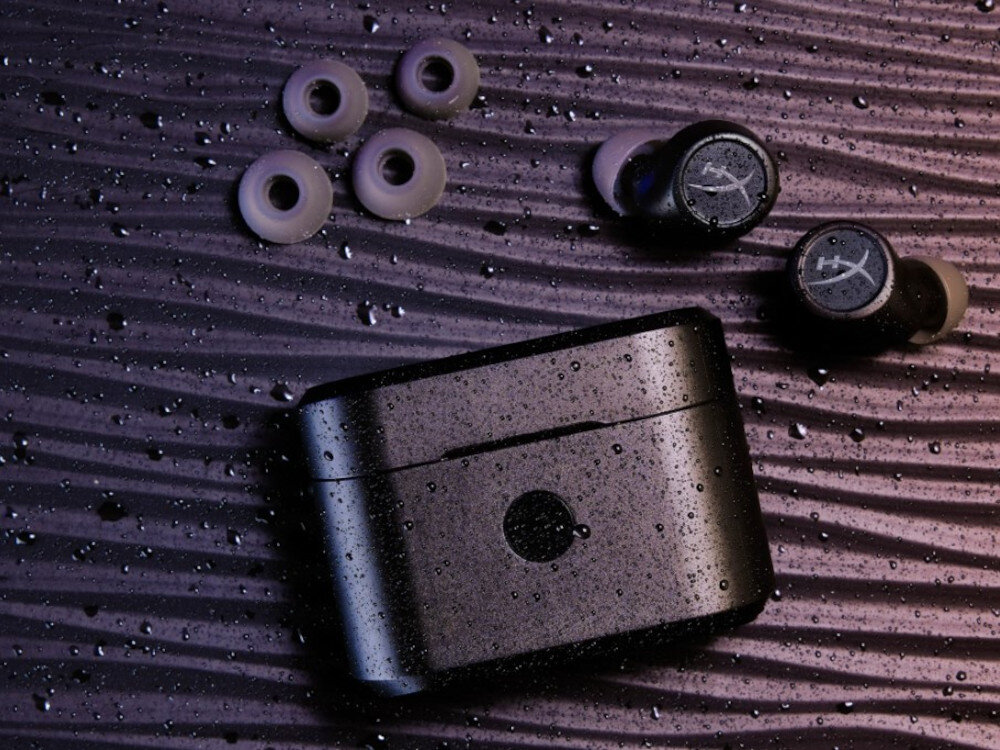 Słuchawki HYPERX Cirro Buds Pro tryb dźwięków otoczenia mikrofony wielokierunkowe wygoda w podróży, słuchawki oraz silikonowe tipsy położone na czarnym blacie