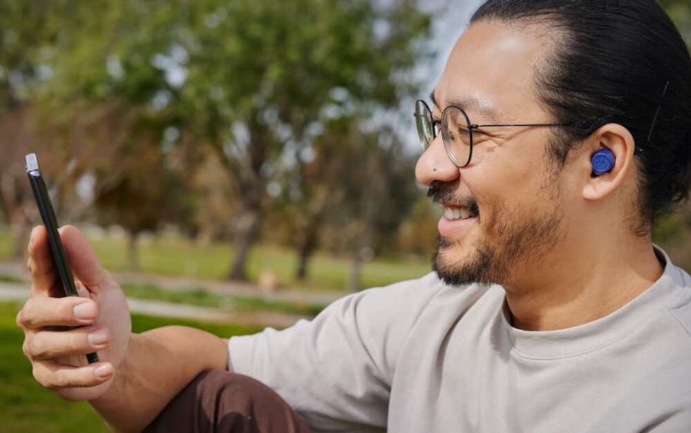 Słuchawki HYPERX Cirro Buds Pro Bluetooth 5.2 stabilne połączenie bezprzewodowe zasięg 10 metrów, osoba z założonymi słuchawkami trzymająca telefon