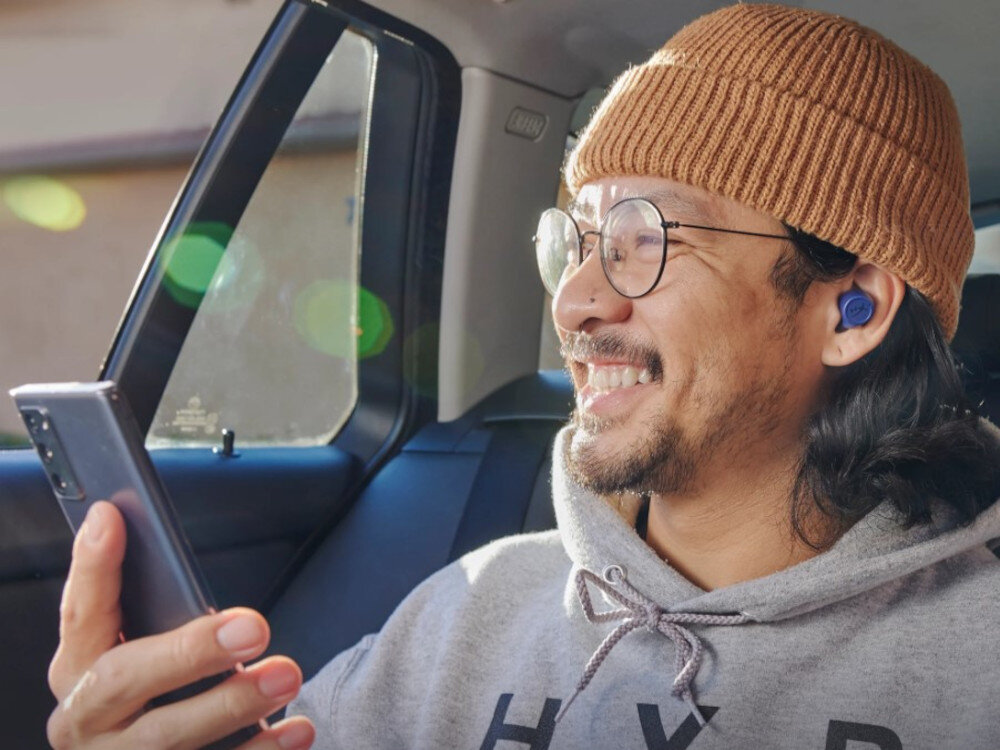 Słuchawki HYPERX Cirro Buds Pro tryb dźwięków otoczenia mikrofony wielokierunkowe wygoda w podróży, osoba z założonymi słuchawkami trzymająca telefon