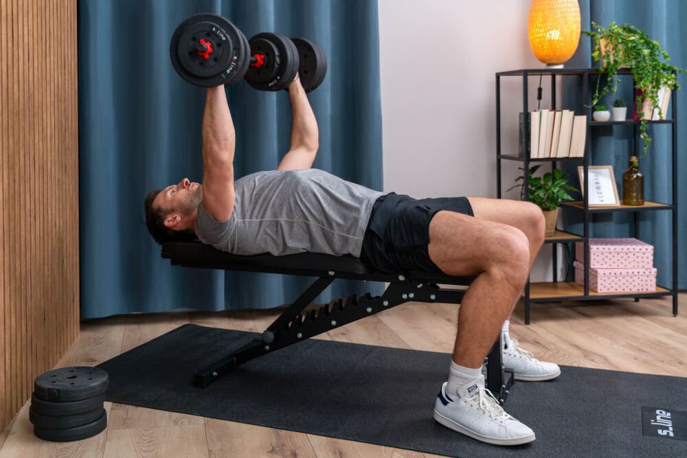 Ławka do ćwiczeń S-LINE ELLI BF300 dla entuzjastow fitnessu solidna wszechstronny sprzed do treningu w domu z mocnej stali o wysokiej jakosci stabilnosc trwalosc dla poczatkujacych dla doswiadczonych Mężczyzna wykonujący wyciskanie hantli na płasko na czarnej ławce treningowej ustawionej w pozycji poziomej.