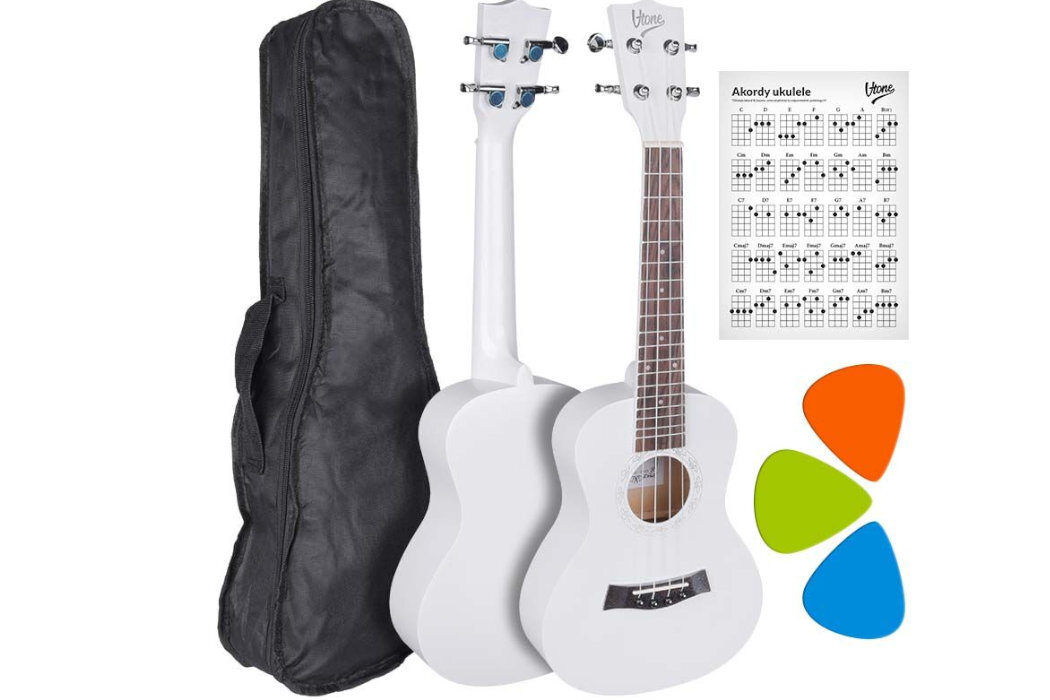 Na obrazie znajduje się białe ukulele koncertowe z brązową podstrunnicą, czarny pokrowiec, zestaw trzech kolorowych kostek oraz karta z akordami ukulele z logo \'V-TONE\'.
