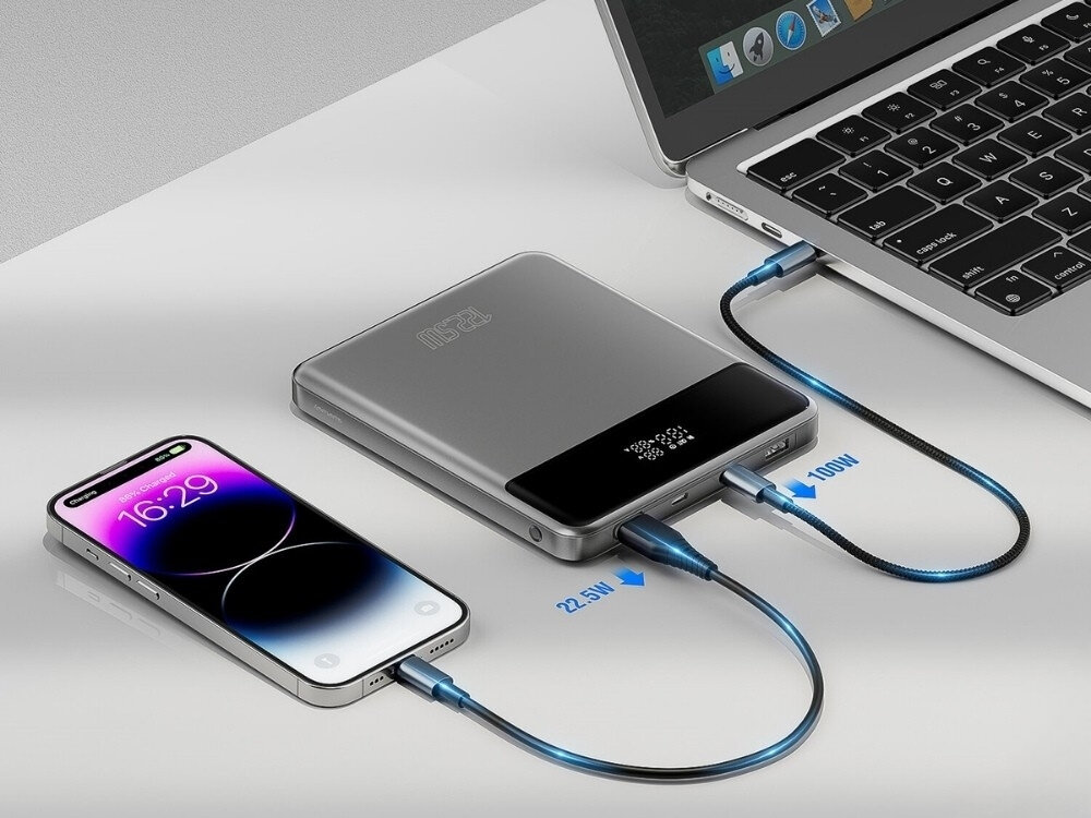 Na obrazie widać szary powerbank podłączony do smartfona i laptopa za pomocą dwóch kabli. Na ekranie smartfona widoczny jest czas 16:29, a przy kablach oznaczenia 22.5W i 100W.