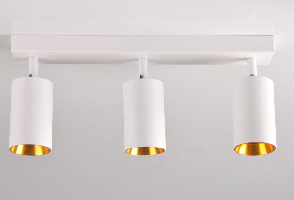 Na obrazie widoczna jest lampa ścienno-sufitowa z trzema białymi cylindrycznymi kloszami, które mają złote wnętrze. Lampa jest zamontowana na prostokątnej, białej podstawie.