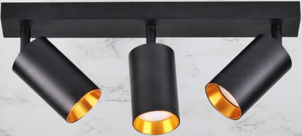 Na obrazie widoczna jest lampa z trzema czarnymi kloszami o złotym wnętrzu, zamontowana na prostokątnej podstawie. Tło jest jasne, przypominające marmur.