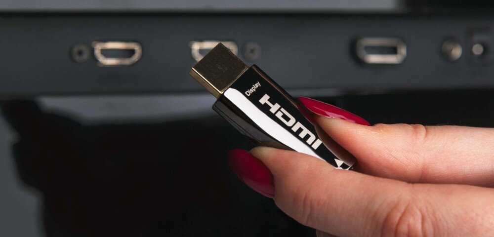 Kabel optyczny HDMI - HDMI CLAROC 70 m odporność na zakłócenia elektromagnetyczne EMI stabilny sygnał, osoba trzymająca kabel w ręku na tle złączy urządzenia