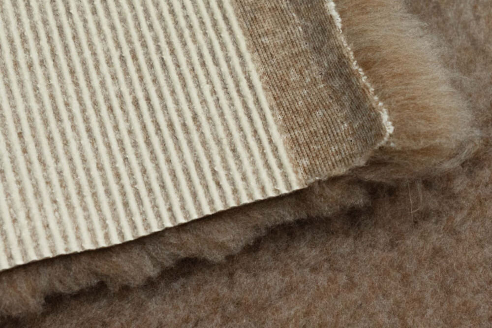 Legowisko uniwersalne BUBA Dry Bed A23 Beżowy 50 x 37 Zbliżenie na róg puszystego, beżowego dywanika. Wyraźnie widoczny jest spód z jasnej tkaniny w prążki oraz krawędź długiego, miękkiego włosia.