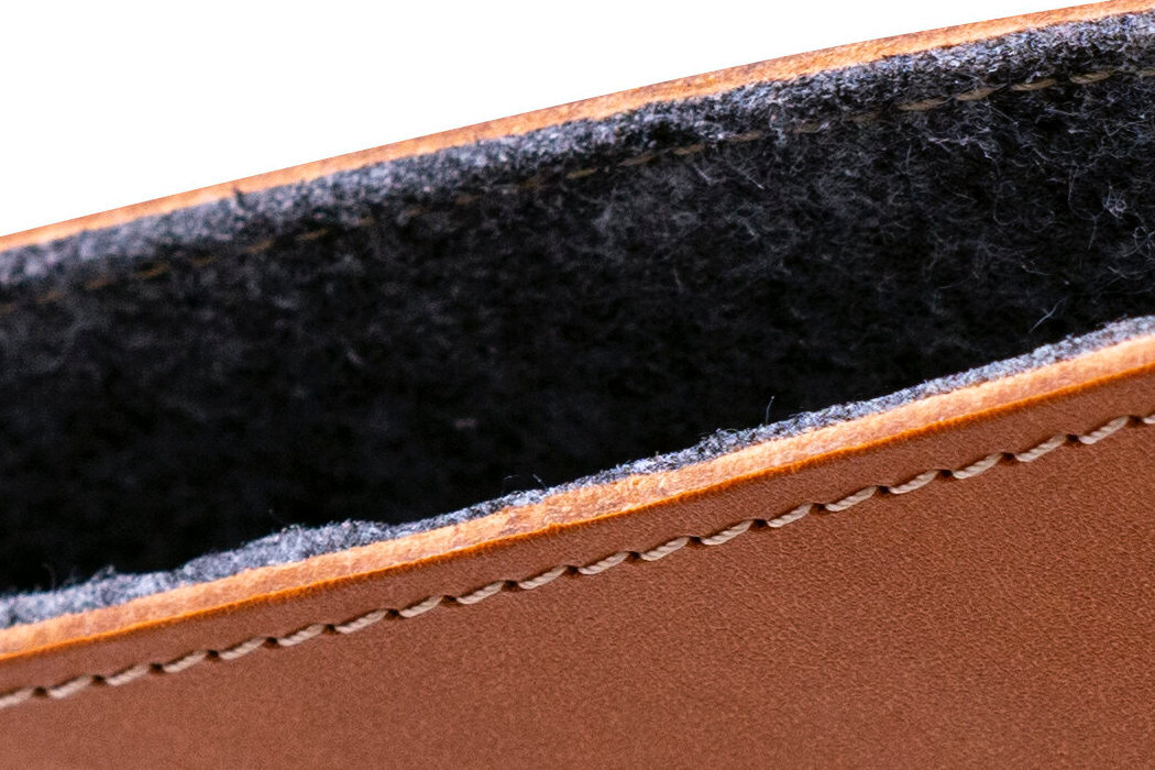 Zbliżenie na brązowe etui z widocznym szwem i ciemnym wnętrzem. Materiał wygląda na skórzany z miękką wyściółką wewnętrzną.