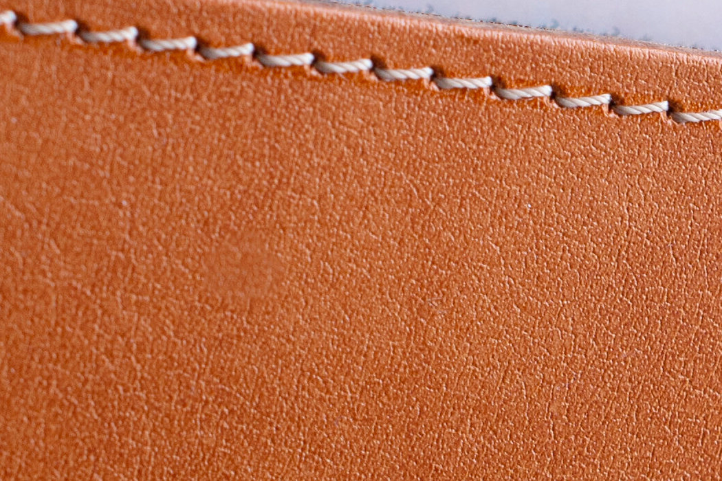 Zbliżenie na brązowy materiał z widocznym białym szwem. Powierzchnia ma delikatną fakturę.