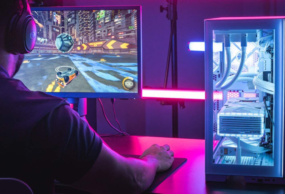 Pamięć RAM CRUCIAL Pro 24GB 5600MHz Osoba z zestawem słuchawkowym grająca w grę wyścigową na monitorze, obok znajduje się komputer stacjonarny z jasnym, białym podświetleniem wnętrza obudowy, działanie, płynność, renderowanie