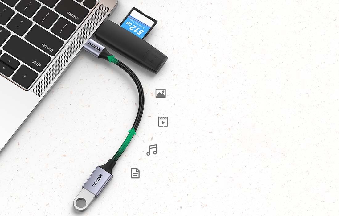 Na obrazie widać laptop z podłączonym adapterem USB-C/USB-A marki Ugreen, do którego włożona jest karta pamięci 512 GB. Obok adaptera znajdują się ikony symbolizujące zdjęcia, filmy, muzykę i dokumenty.
