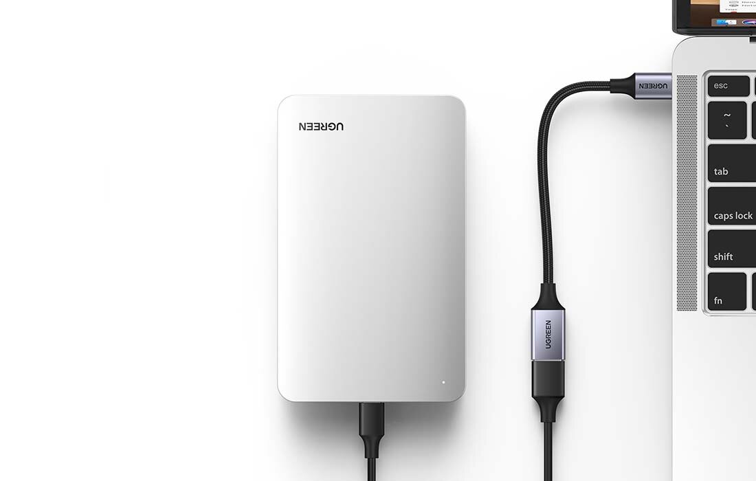 Na obrazie widoczny jest srebrny dysk zewnętrzny z logo \'UGREEN\', podłączony do laptopa za pomocą czarnego kabla USB z napisem \'UGREEN\'.
