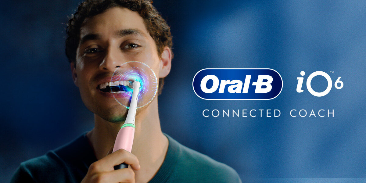 Osoba używa różowej szczoteczki magnetycznej Oral-B iO 6. Obok widoczne jest logo \'Oral-B iO 6\' oraz napis \'CONNECTED COACH\'.