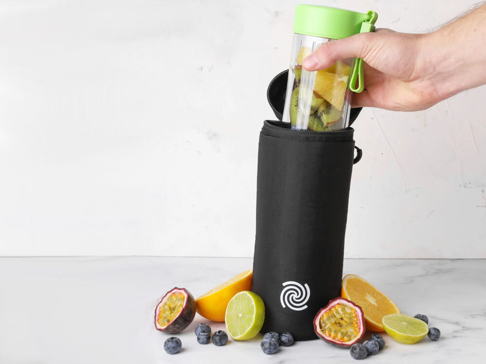 Etui termiczne BLENDYGO do BlendyGo 3 czarne etui jasne tło osoba wkłada blender z zieloną zakrętką do czarnego etui obok leżą rozkrojone owoce dla entuzjastów koktajli warstwa izolacyjna optymalna temperatura napoju przez wiele godzin orzeźwiające zimne koktajle komfort funkcjonalność
